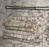 All necklaces and chains arranged on a grey velvet surface showing variety of materials and styles including stone beaded necklace missing clasp and gold-tone clover pendant