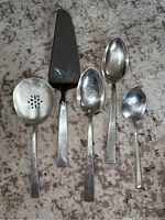 Top view of five sterling silver serving pieces on a textured surface.