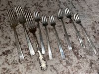 Top view of nine assorted sterling silver forks laid in a row showing different sizes and handle designs including one ornate floral handle fork.