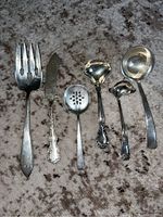 Six sterling silver serving pieces arranged side by side on carpet