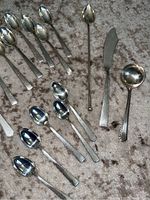Top-down view of flatware pieces arranged on carpet, showing spoons, fish knife, ladle, sugar spoon.