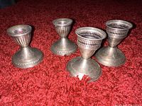 Front and side view of both pairs of sterling silver candle holders on red carpet, showing fluted designs and pierced collar on one pair.