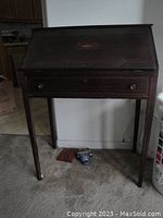 Front view of closed antique secretary desk showing dark wood finish, decorative wood inlay on drop-front panel, and simple knob handles.