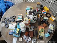 Wide view showing a variety of camera accessories including lens caps, boxed filters, adapters, and other small parts spread on a round table.