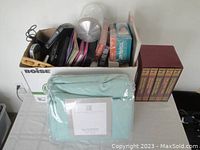 Box with various electronic devices, VHS tapes and five hardcover books in brown covers