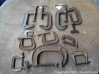 Photo showing entire collection of 11 metal C clamps of various sizes and brands on wooden surface.