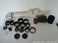 Various lens hoods, lens filters, extension tubes, lens caps, leather cases, and soft cylindrical case arranged on table surface.