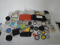 Overview of assorted camera lens filters, cases, and accessories laid out on a white surface, showing filters with colored glass and rings with and without glass.