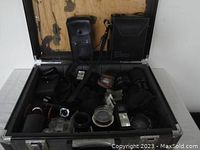 Open metal Halliburton hard case filled with assorted camera accessories including lenses, flash components, and pouches.