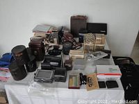 Table covered with brown and black camera cases, accessory boxes, owner’s manuals, Canon hard case and Canon 110ED kit
