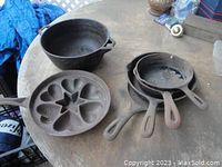 Top view of four cast iron skillets of varying sizes, a cast iron baking muffin pan with heart-shaped molds, and a small cast iron bowl all placed on a wooden surface.