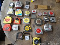 Photo showing an assortment of various tape measures laid on a table including pocket tape measures, carpenter folding tape, long winding tape, and wooden folding ruler segments.