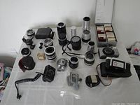 Wide view of collection on table showing various camera lenses in multiple sizes, cameras, accessories and slide holder with photographic slides