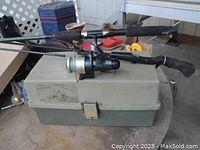 Photo showing two fishing rods with reels resting on a beige and green hard plastic tackle box.