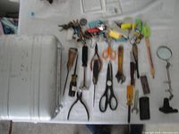 Halliburton metal case with various small hand tools laid out on a surface including scissors, pliers, awls, and screwdrivers.