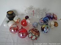 Overview of multiple assorted handblown glass Christmas ornaments in various shapes and colors including balls, snowmen, and a textured beadwork ornament.