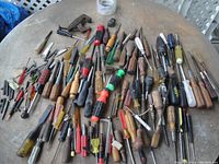 Top view of a large collection of screwdrivers, nut drivers, chisels, various driver bits, and other hand tools spread on a table.