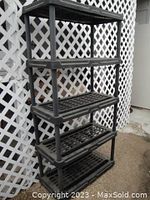 Five-tier black plastic storage rack shown from the front angle against the white lattice background, clearly showing structure and shelf design.