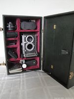 Open green leatherette case showing camera body and accessories in red velvet compartments