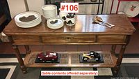 Full view of the oak console table showing top surface, drawer, and lower cane shelf with collectible cars beneath.
