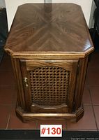 Front view of the octagonal oak side table with decorative veneer top and closed cane webbing door with brass handle.
