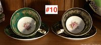 Two porcelain teacups with matching saucers, one green and one black, both with gold decoration and floral design inside the cup.