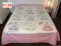 Full view of double size quilt spread on bed showing pink border and white central panel with appliquéd vintage dress motifs.