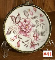 Front view of round porcelain dresser dish showing pink floral design and gilt brass frame.