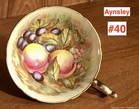 Top-down view showing the hand-painted fruit design inside the teacup with peaches, grapes, and leaves.