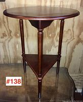 Side view of side table showing height, three legs, triangular base, and smooth finish. Glass surface and wooden wall background.