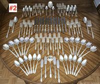 Full view of flatware laid out on a table showing the complete set arranged by type showing knives, forks, spoons and serving pieces.
