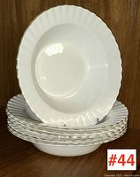 Side view stack of six white soup plates with scalloped edges and gold trim, with one plate displayed vertically to show shape.