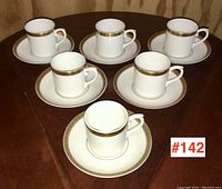 Set of six porcelain demi-tasse cups and matching saucers arranged on wood table.