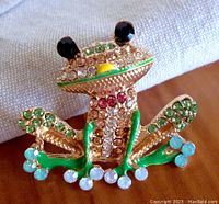 Close-up front view of the frog brooch showing details of rhinestones and enamel along the face and limbs.