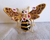 Front view of the gold-tone bee brooch showing purple rhinestones on wings and pink enamel flowers.