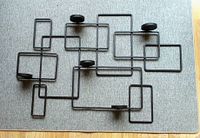 Full view of large geometric wrought iron wall decor piece with five circular platforms for votive candles, laid flat on gray fabric background.