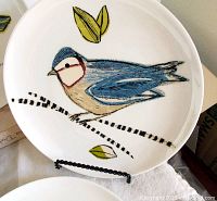 Close-up of porcelain plate featuring a blue bird on a branch with yellow leaves, showing hand-painted details.