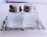 Front view of hobnail glass salt and pepper shakers on ornate silver-plated tray, showcasing textured glass and polished tops.