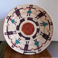 Front view of large colorful tribal gathering basket showing human figure motifs and central spiral design.