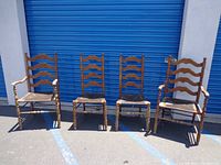 Four vintage wooden dining chairs with woven seats and ladder back design, set against outdoor blue metal door.