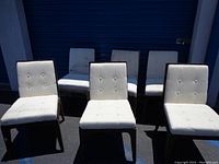 Six beige upholstered dining chairs arranged in two rows, visible dirt and stains on the fabric upholstery.