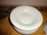 Stack of 8 white soup plates showing embossed grapevine pattern on rim.