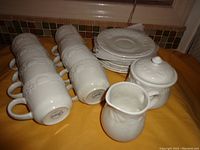 All 8 cups, 8 saucers, creamer, and sugar bowl with lids arranged on a surface showing grapevine embossed design