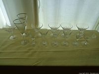 Set of 12 assorted clear glassware glasses displayed in a row on a yellow tablecloth in front of a curtain.
