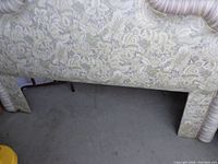 Close image of the lower portion of the upholstered headboard showing the floral lavender and beige fabric and the striped fabric wrapped legs.