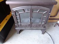 Front view of the stove-style electric heater with closed double glass doors and decorative metal detailing.