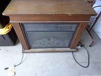 Front view of electric fireplace heater showing wooden mantel, vent control panel, glass front with faux logs, and power cord