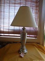 Complete lamp with silver metal base and beige fabric shade under daylight.