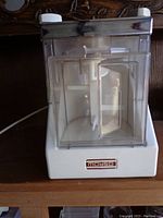 Front view of clear plastic mixing container with internal mixing paddle attached to white electric base.