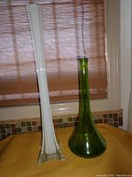 Full view of two vases showing relative size and shape, white and green glass vases on orange surface with window blinds background